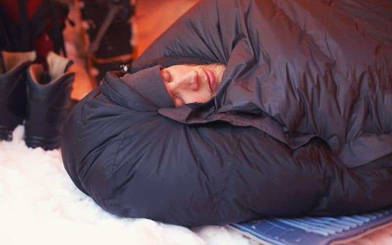 Man sleeping in down sleeping bag beside snow