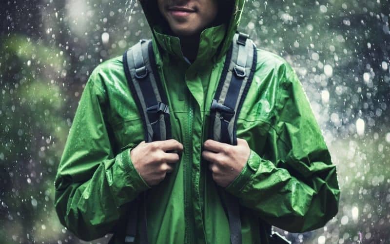 Man standing in rain with rain jacket on and holding the straps of his backpack