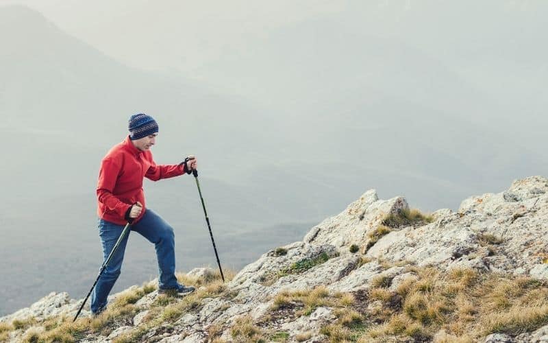 Man using trekking poles-to-walk uphill over rocky terrain