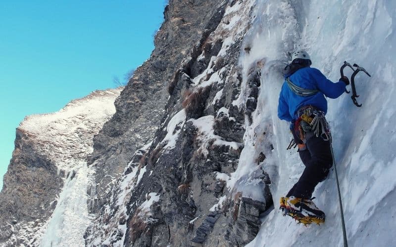 Man wearing ice boots and crampons climbing up vertical ice face