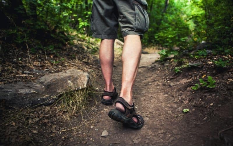 Man wearing sandals walking on well trodden path through forest