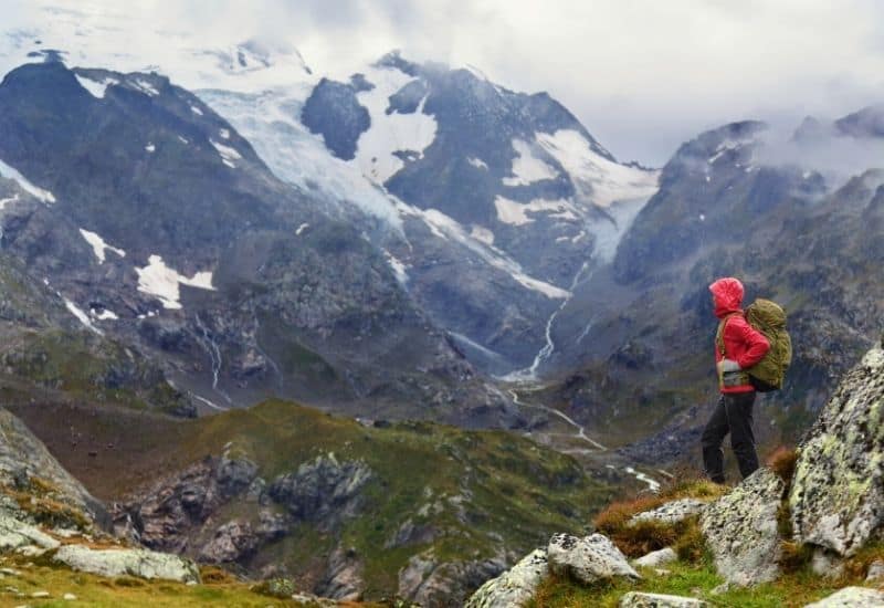 Person with red lightweight rain jacket on looking at mountains - featim