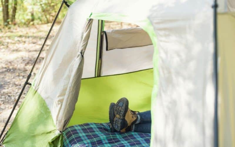 The entrance of a tent where a persons feet can be seen at the end of a mattress inside