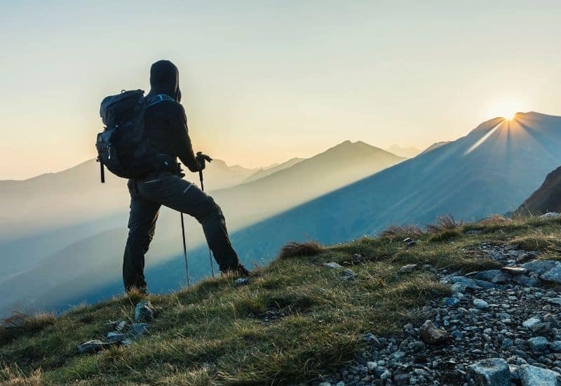 Man with trekking poles looking at sunrise over mountains