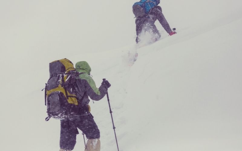 Two hikers climb a snowy slope with walking poles