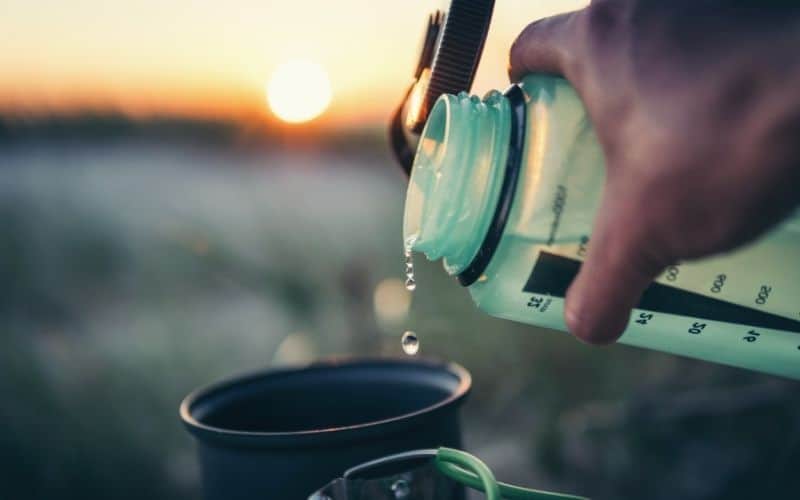 Water being poured into camping stove pot as the sun rises