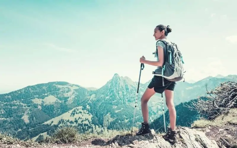 Woman holding walking poles and carrying a backpack looking out over mountains