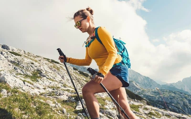Woman in long sleeved top and trekking poles climbing uphill