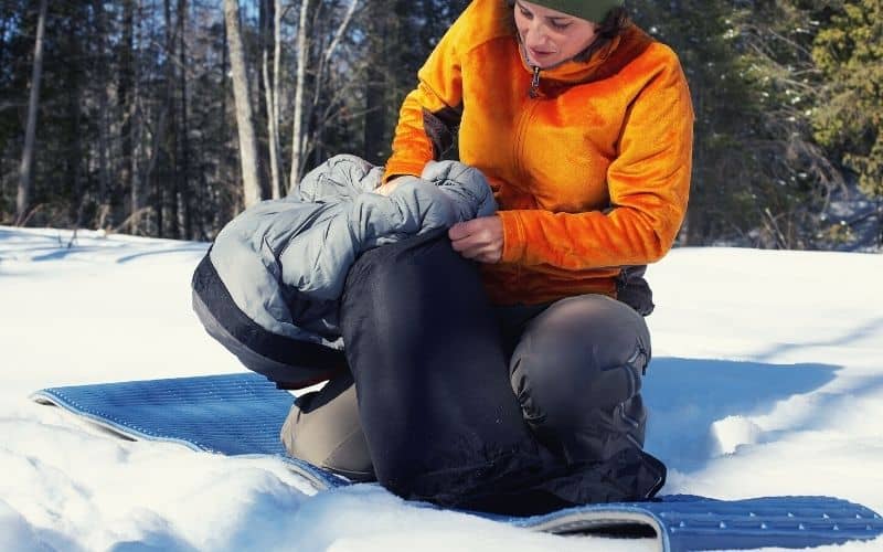 Woman stuffing sleeping bag into stuff sack in the snow