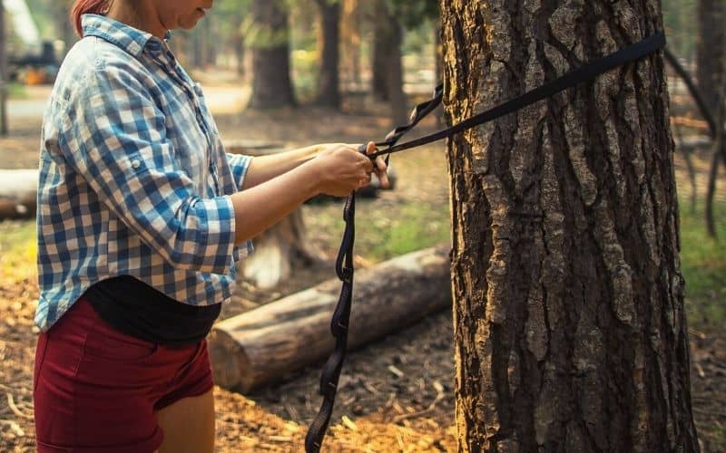 Woman tying daisy chain hammock strap to tree