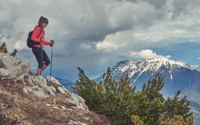 Woman with trekking poles hiking downhill over rocky terrain