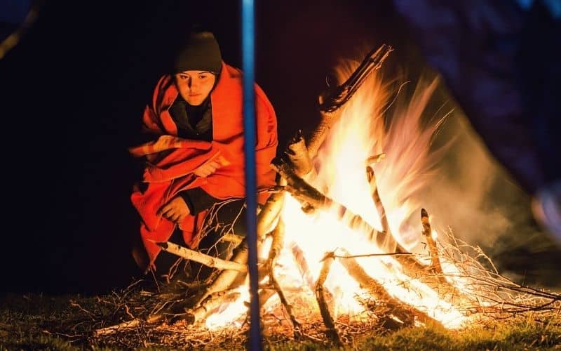 Woman wrapped in blanket in front of a campfire