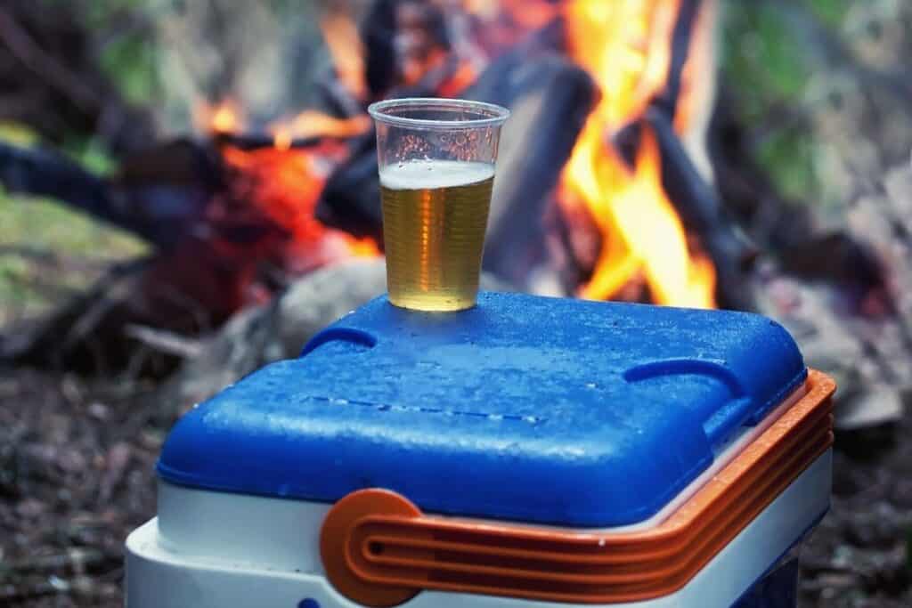 Camping cooler sitting in front of a campfire with a beer on top