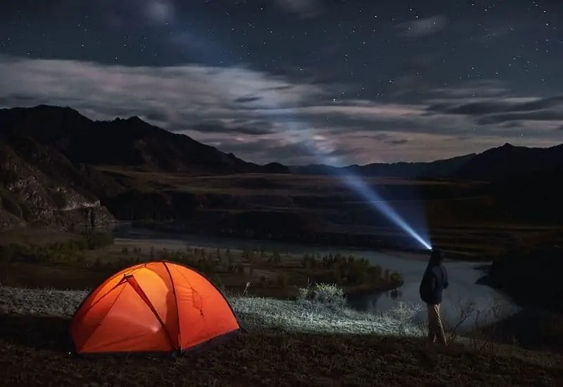 Man beside tent shining flashlight into the night sky