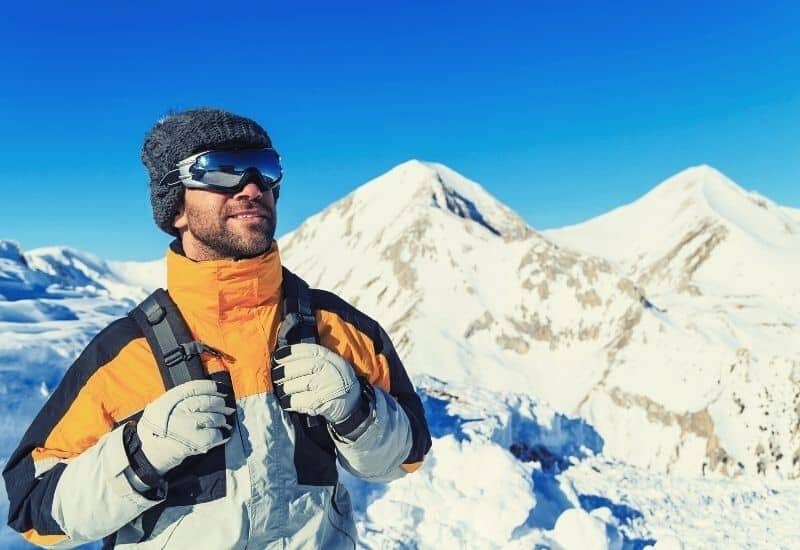 Man in snowy mountains wearing winter gloves and goggles