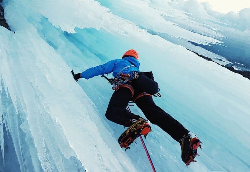 Looking up at a man wearing ice boots with crampons while climbing a frozen waterfall