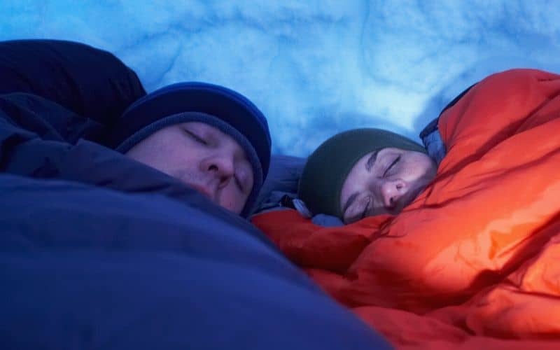 Campers in sleeping bags sleeping in snow