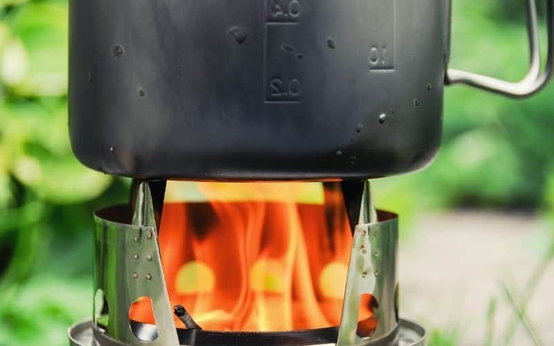 Flames of a wood burning camp stove heat a pot above it