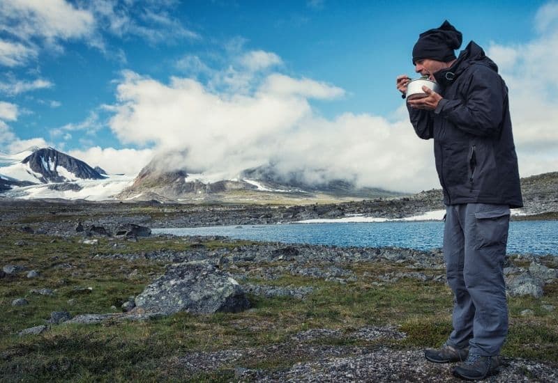 Hiker eating out of a bowl in front of a lake