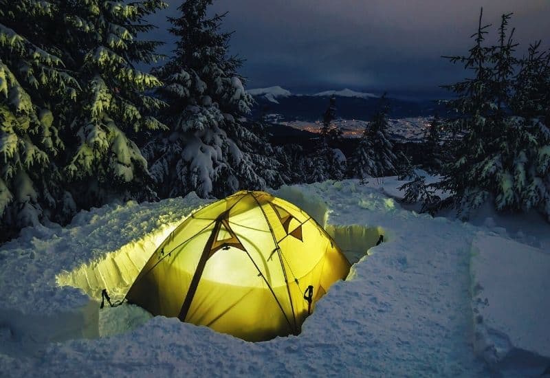 Tent pitched in deep snow overlooking a city in the ditance