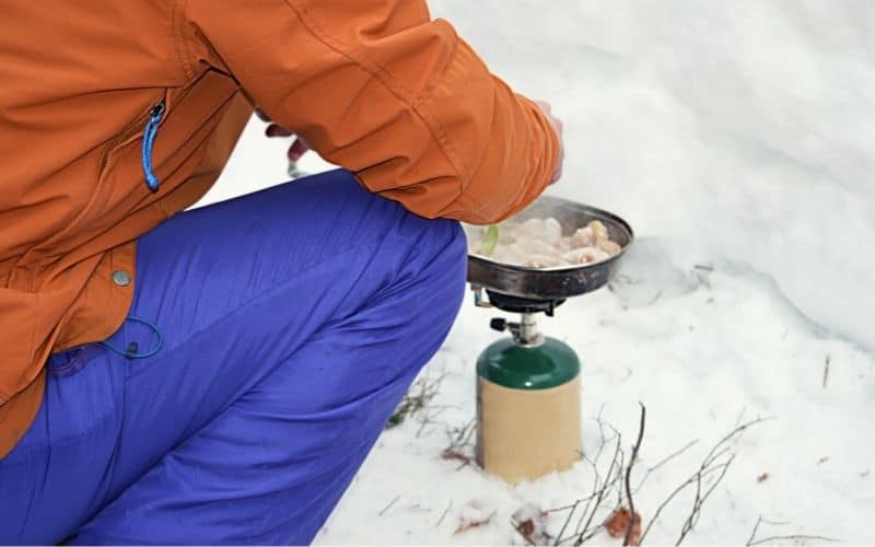 Man cooking food over propane gas stove in the snow