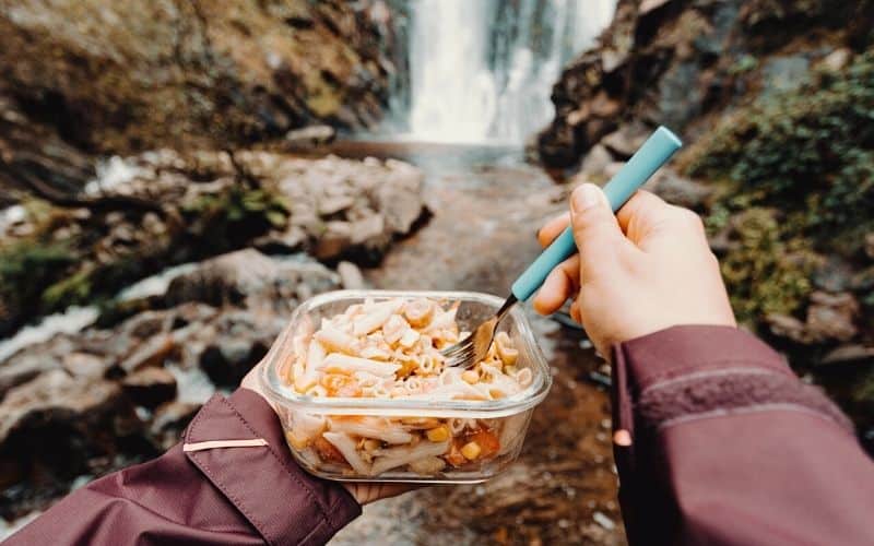 Person eating pasta in front of a waterfall