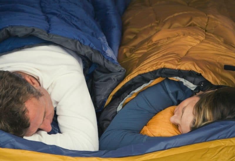 A couple sleeping in a sleeping bag and one with a quilt