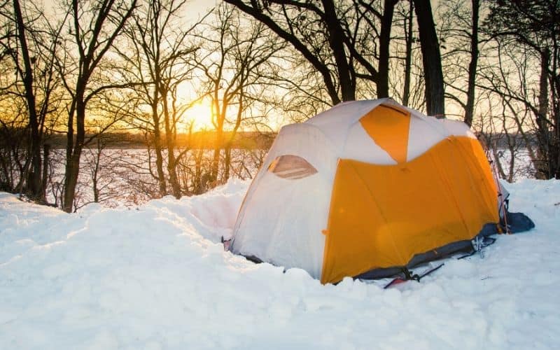 Tent pitched in snow with a snow windbreaker surrounding it