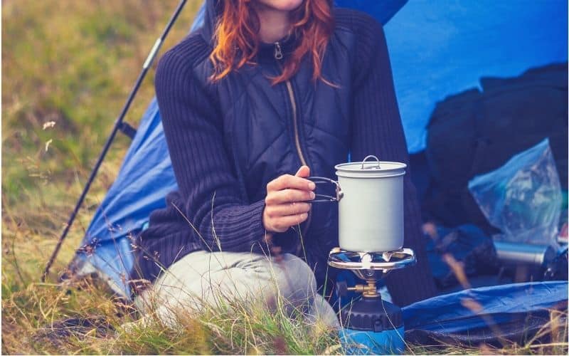 Woman cooking on a propane burner in front of her tent