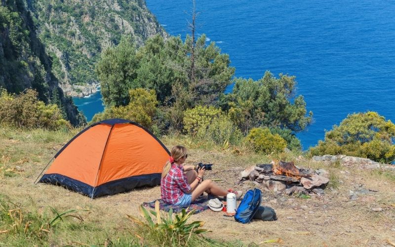Woman sitting beside tent and a campfire on clifftop