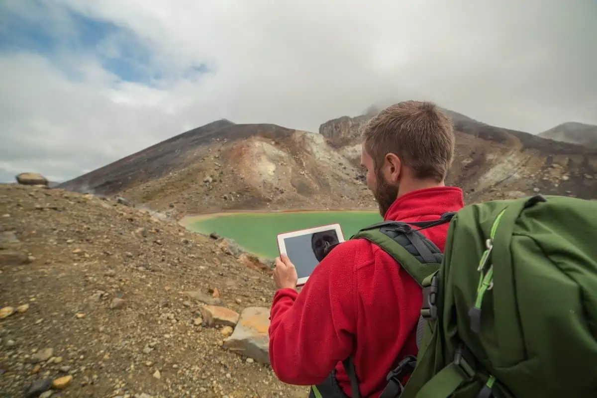 Man using a tablet to naviagte in front of a crater lake