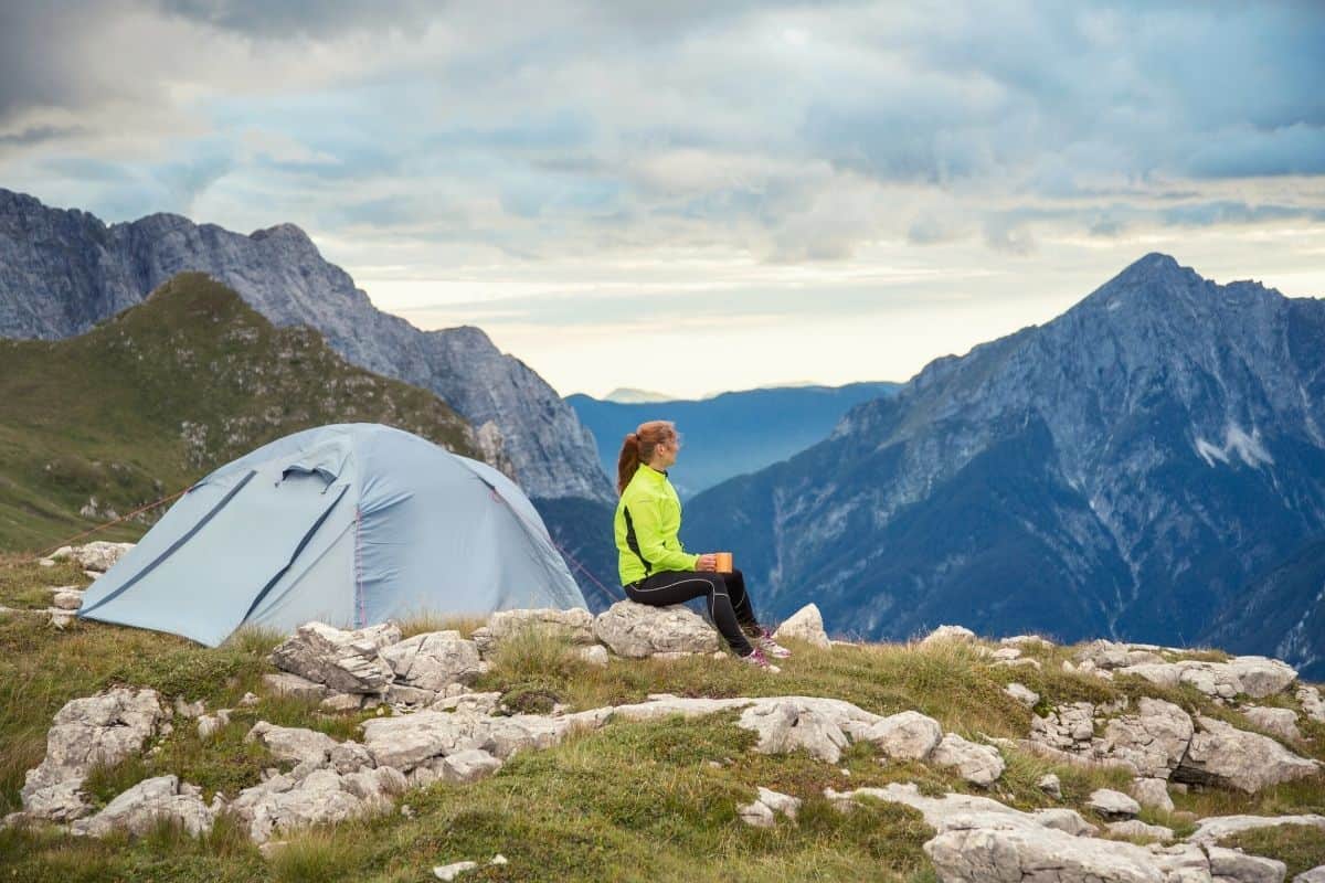 Woman sitting beside a tent looking out over mountains