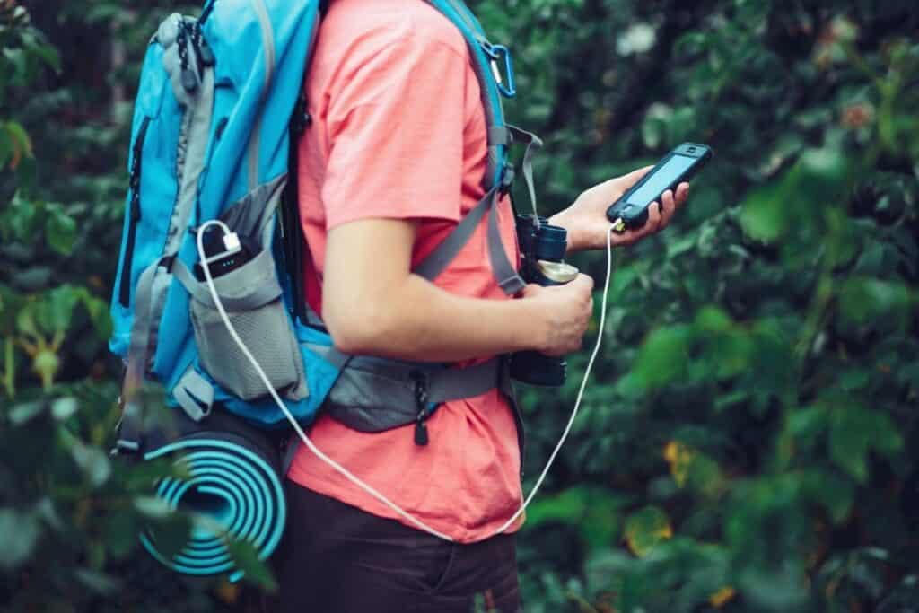 Backpacker charging phone from a power bank in his backpack side pocket as he walks