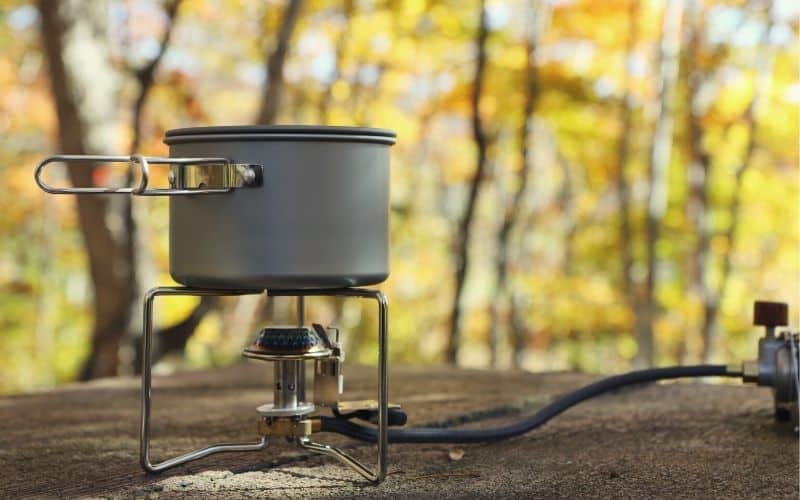 Camp stove connected to fuel with liquid gas line on flat surface