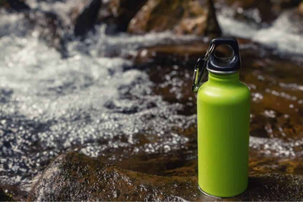 Green metal water flask sitting on rock in front of a river