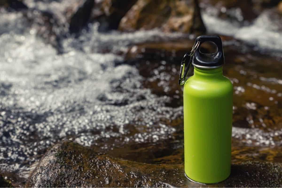 Green metal water flask sitting on rock in front of a river