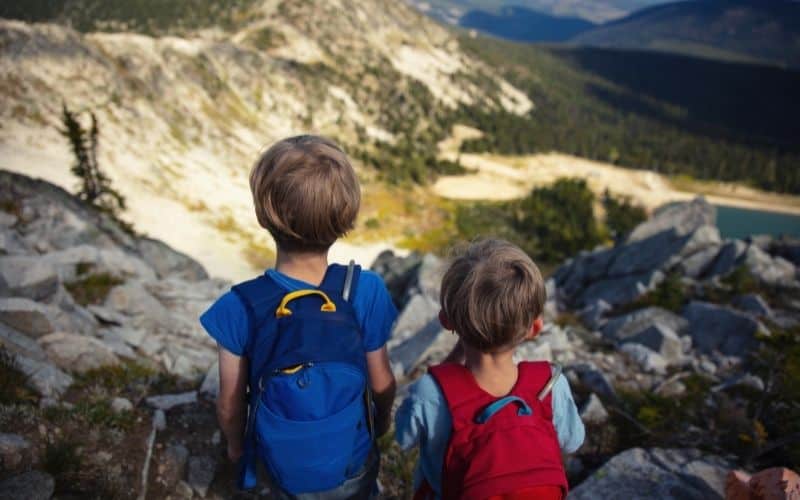 Kids wearing backpacks looking at a lake from a mountaintop