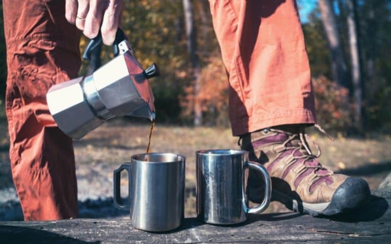Man in hiking boots pouring coffee into metal mugs