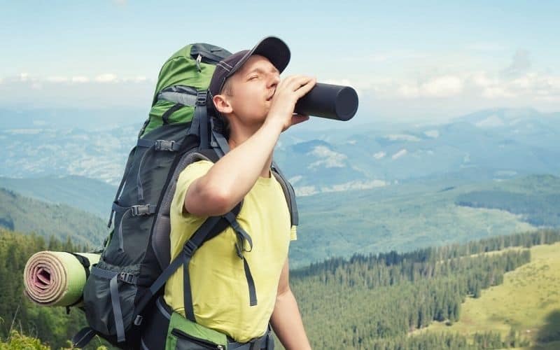 Man on hike with camping gear on his back drinking from flask