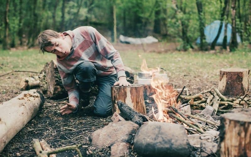 Man starting a campfire with his tent in the background