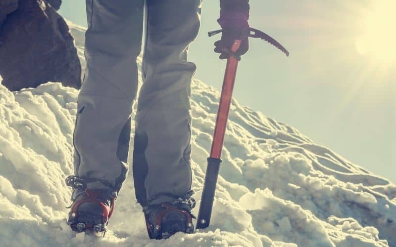 Person hiking in snow wearing crampons and holding an ice axe
