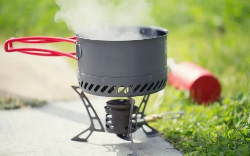Pot of water boiling over a liquid gas camp stove resting on a flat surface