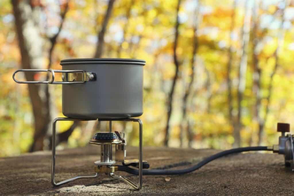 Camping stove connected by a fuel line to a white gas canister