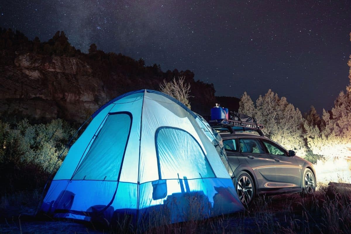 SUV tent attached to car lit up under a starry night