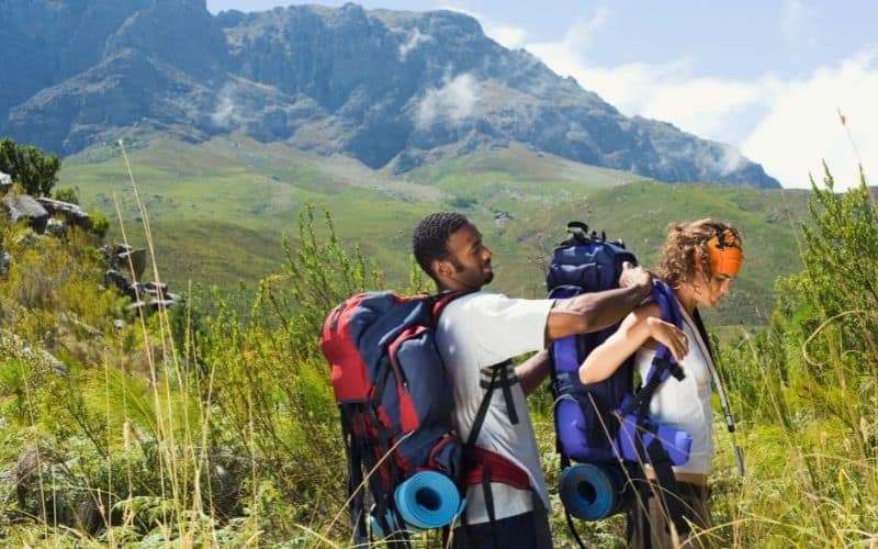 Hiker helping another hiker put on heavy backpack