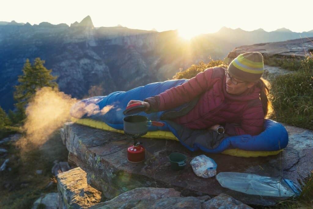 Woman lying in sleeping bag beside backpacking stove