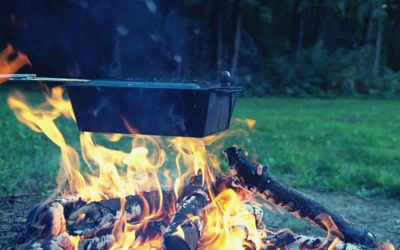 Popcorn cooking over a campfire in a popper with extended handle