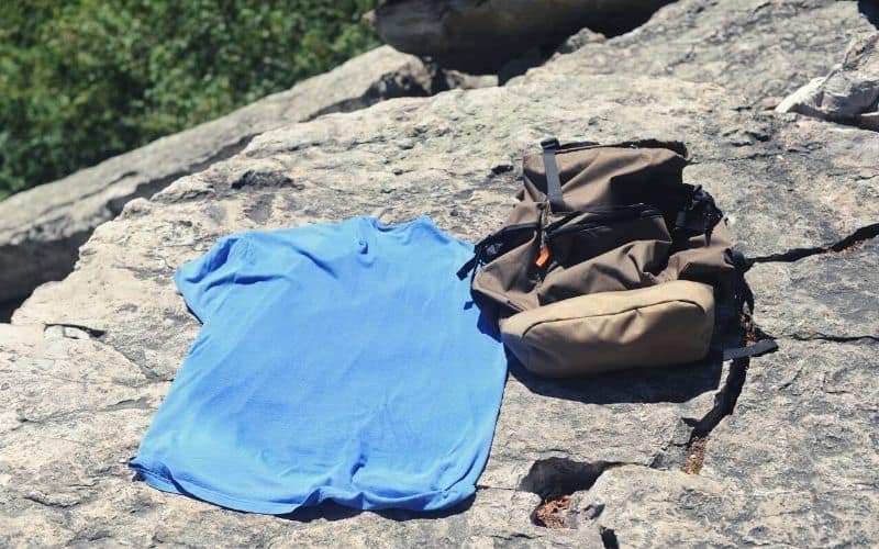 Sweaty t-shirt and backpack lying in the sun on rocks