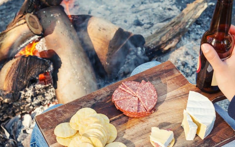 Camper in front of campfire with a board of cold meat and cheese