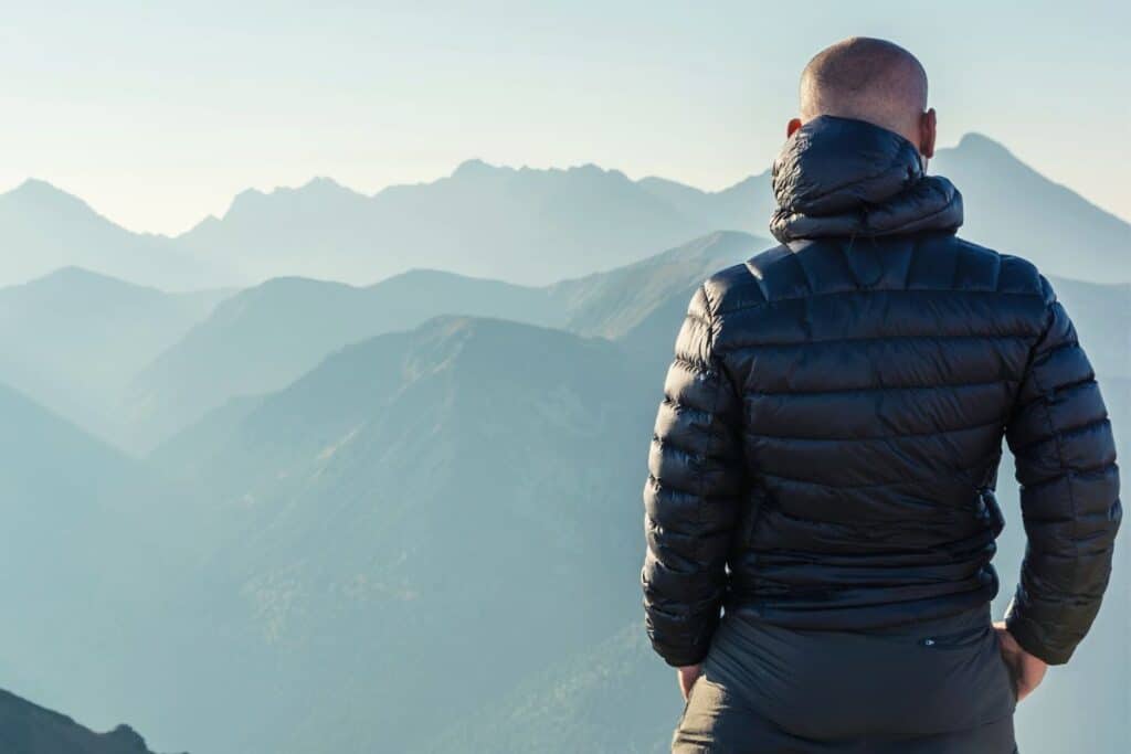 Man wearing down fill jacket looking out over mountains